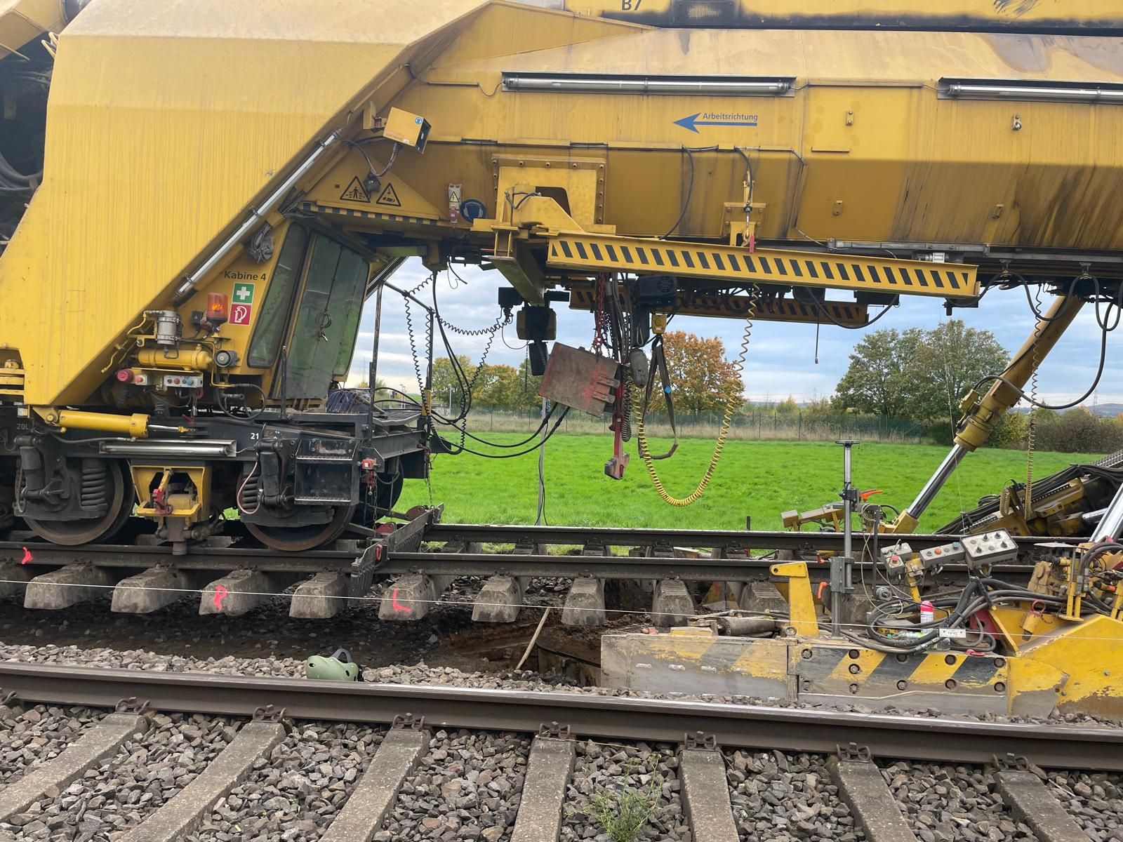 Gelbe Gleisbaumaschine über Schienen und Betonschwellen in seitlicher Ansicht.