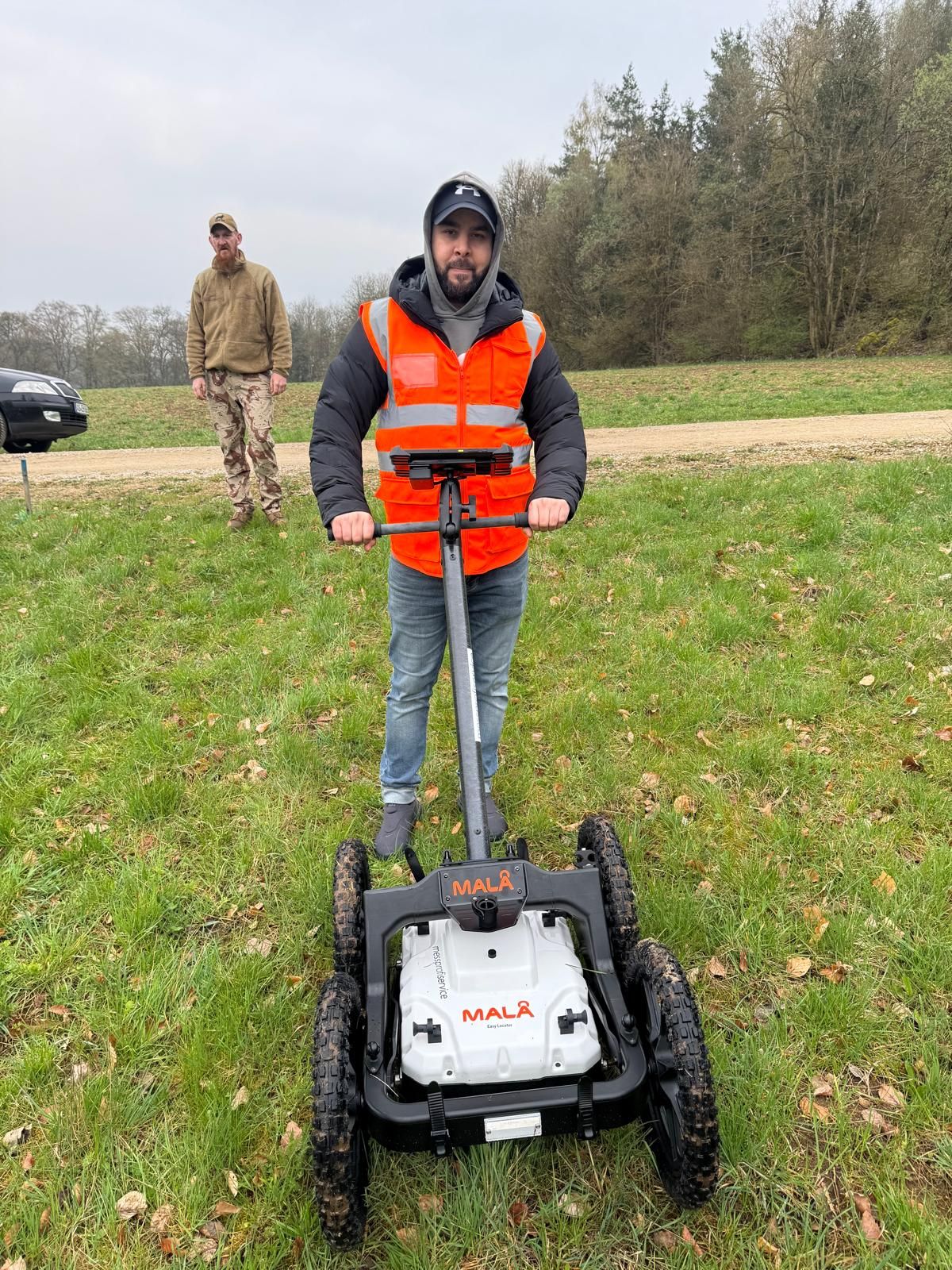 Person in orangefarbener Warnweste mit einem MALÅ-Messwagen auf einer Wiese