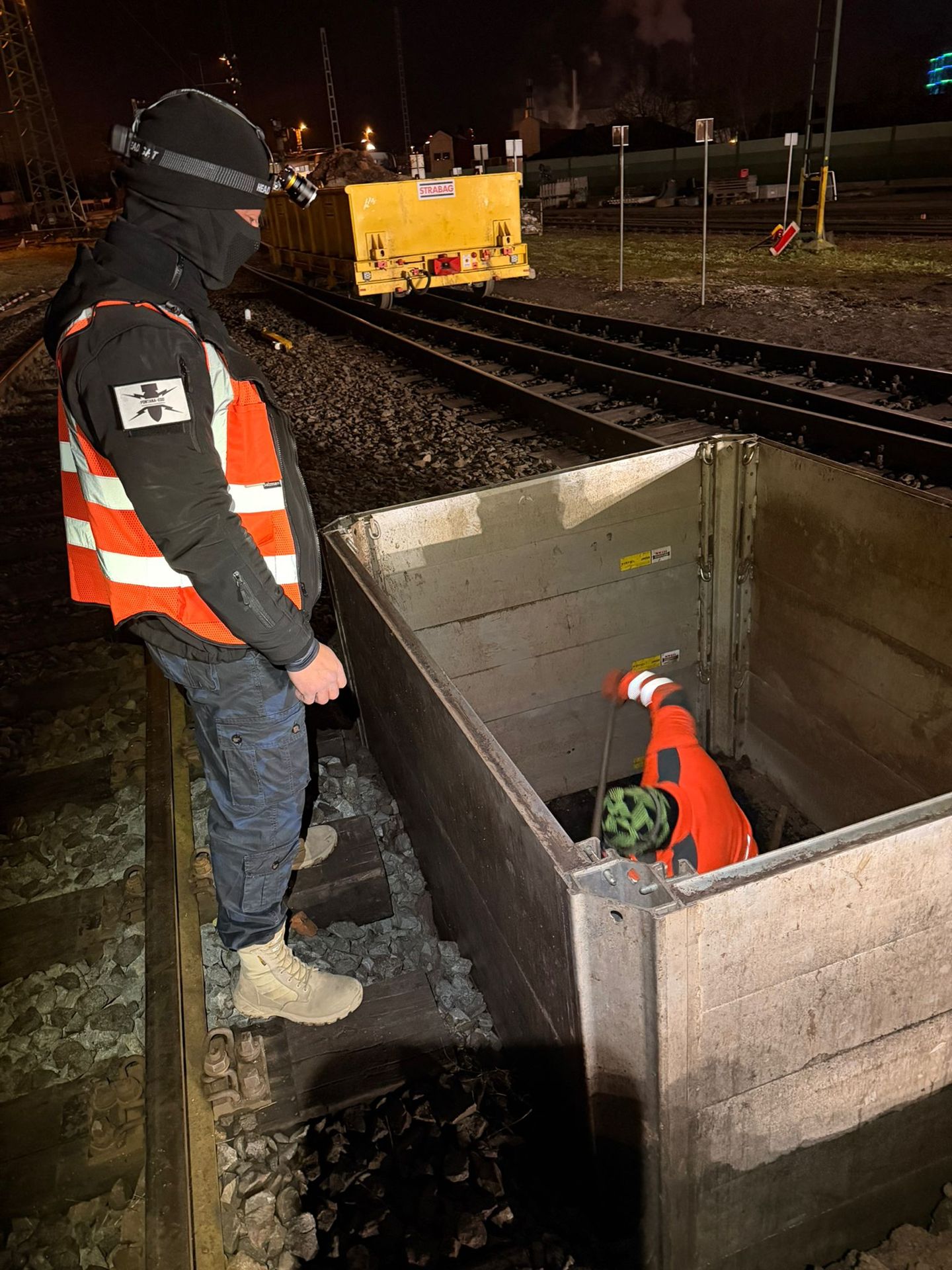 Personen neben und in einem Verbau im Gleisbereich bei Nacht.