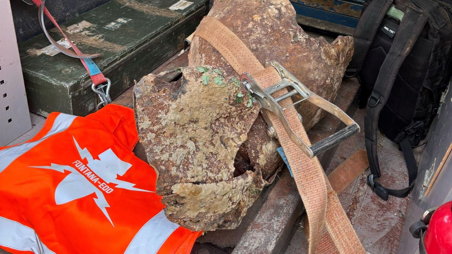 Bombenkörper mit Spanngurt und orangefarbener FONTANA-EOD-Warnweste in einem Fahrzeug.